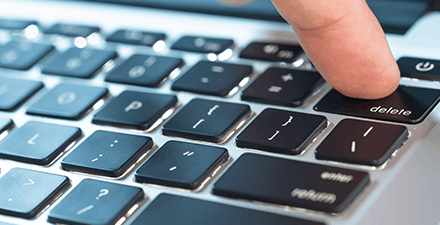 Finger of the computer user, he presses the delete button on the computer keyboard.