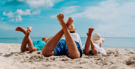 A man and w children lying on their stomachs on the beach looking at the ocean.