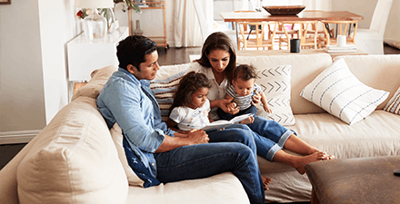 Family sitting on sofa reading a book together in the living room