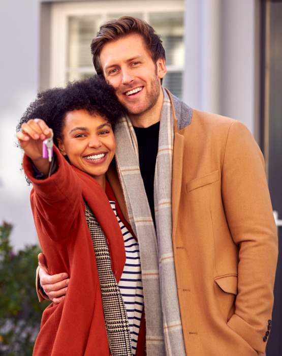 a couple hugging while holding keys to a new house