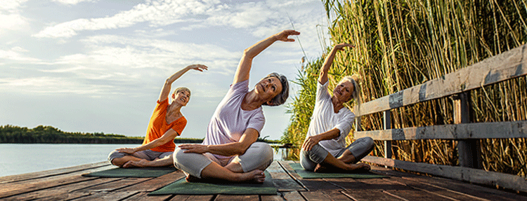 Group of retired teachers practicing yoga lakeside.