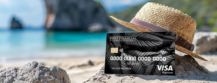 Platinum Visa credit card on the sand, leaning on a straw hat on the beach.