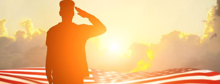 Soldier saluting the USA flag as the sun rises in the background–Veterans day holiday.