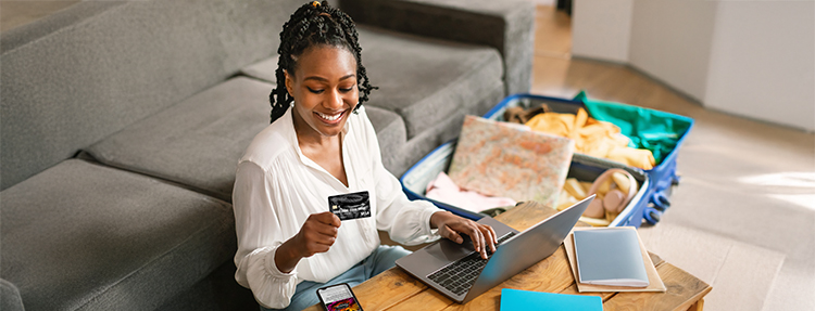 Happy African American woman using her credit card to book travel.
